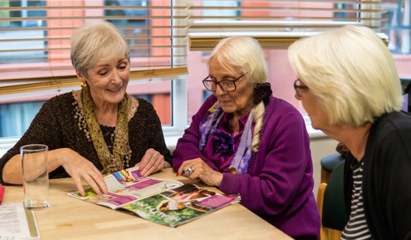 Group Of Older Women Sitting Together At A Table Looking At A Magazine