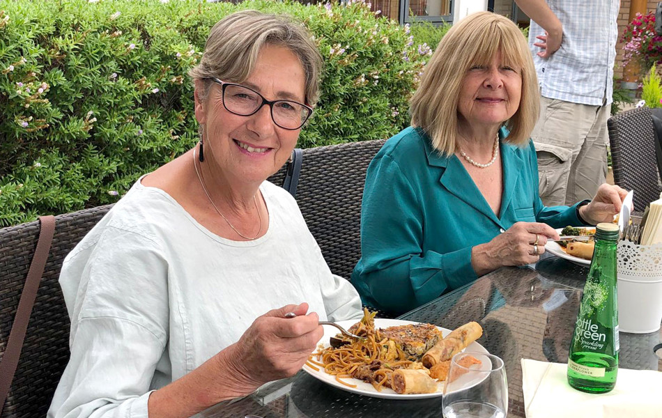 Two ladies at Girton Green sitting outdoors eating food from a Vietnamese buffet