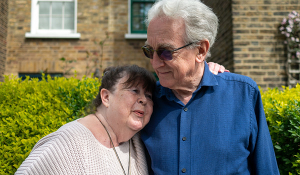 Older Woman Resting Head On Older Man's Shoulder In Street
