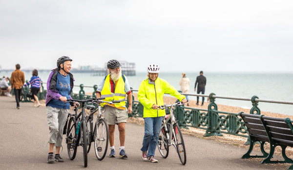 Group Of Older People Pushing Bikes On Sea Front