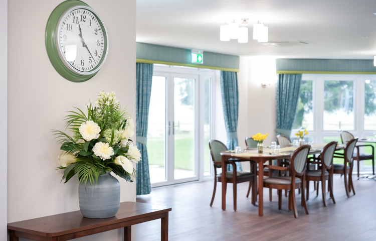 Bright and welcoming dining room at Westall House Residential Care Home in Horsted Keynes, with set tables, comfortable chairs, and a large clock on the wall.