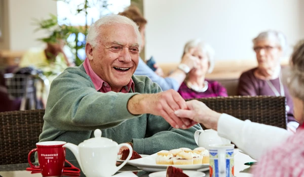 Smiling Older Man Enjoying Tea And Cakes With Others