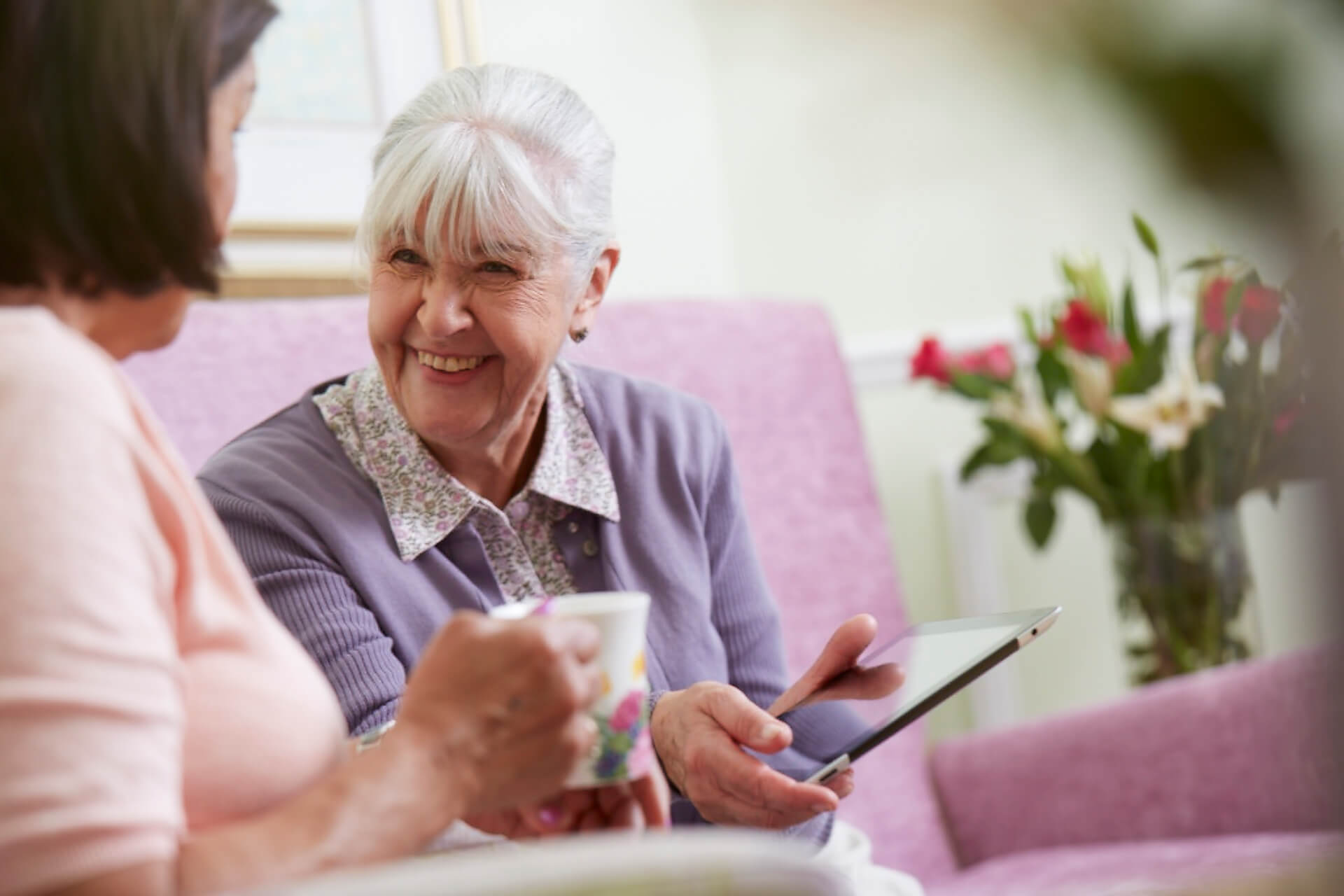 Smiling older lady showing friend her tablet