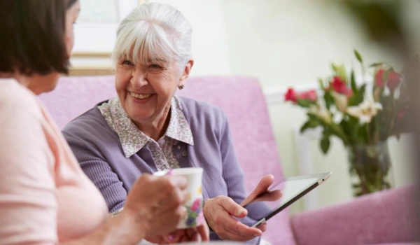 Smiling older lady showing friend her tablet