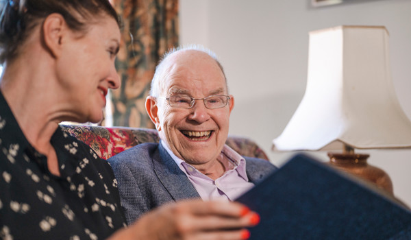 Smiling Older Man And Woman Sitting On Sofa Looking At Photo Album
