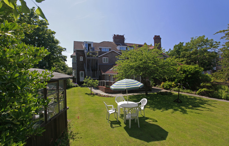 A large bright garden surrounded by trees and a patio set on the grass