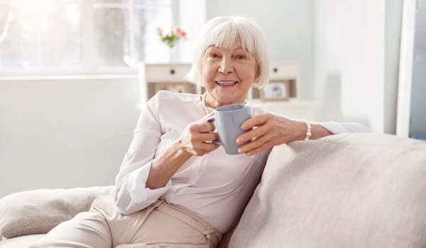 Older Woman Sitting On A Sofa With A Cup Of Tea