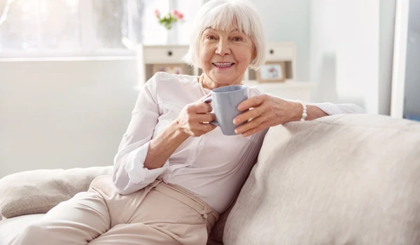 Older Woman Sitting On A Sofa With A Cup Of Tea