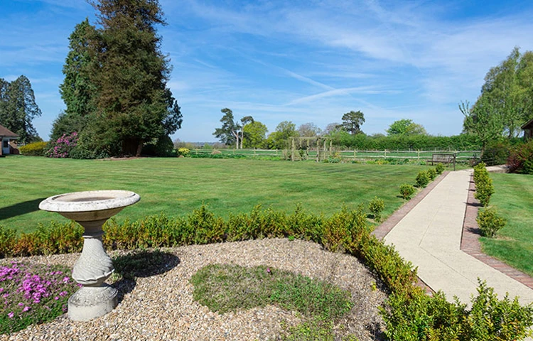 Beautiful gardens at Westall House Residential Care Home in Horsted Keynes, featuring a large lawn, trees, and a paved pathway.