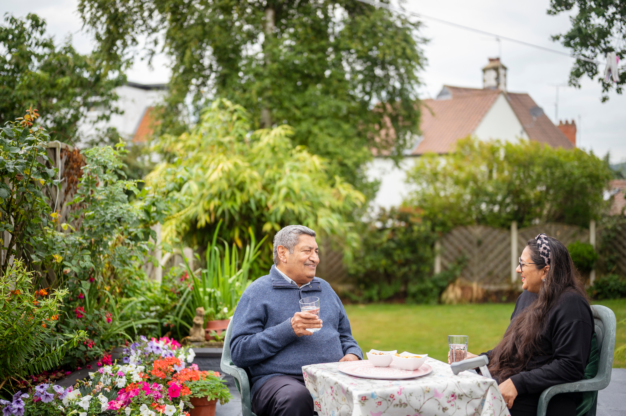 Older Man And Woman Sitting At A Table In A Beautiful Garden