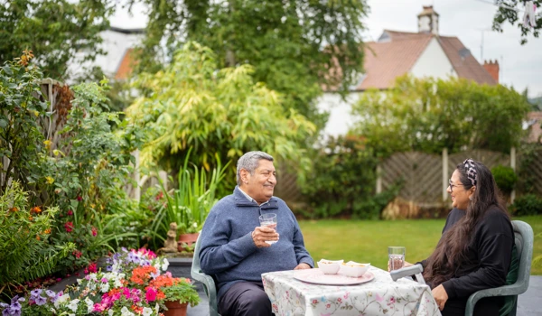 Older Man And Woman Sitting At A Table In A Beautiful Garden