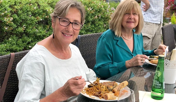 Two Older Ladies Sitting Outside Enjoying A Meal Together