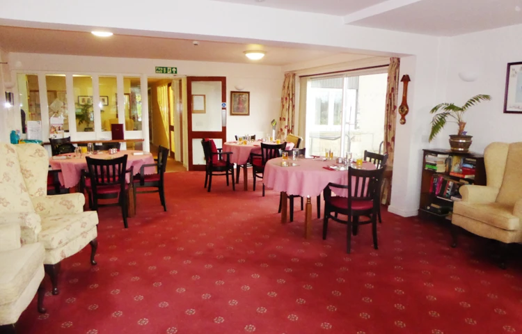 Bright dining area with red carpet and round tables at Abbeyfield House sheltered housing in North Yorkshire